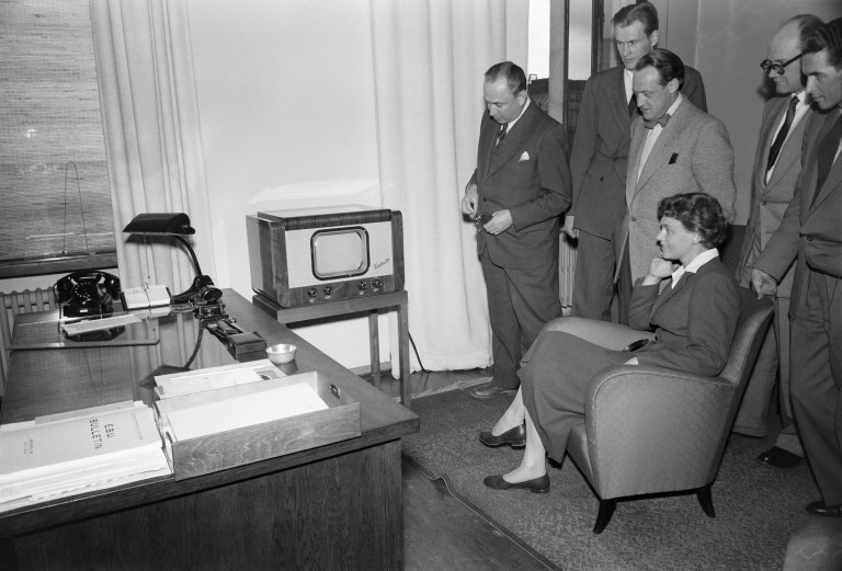 Mustavalkoinen kuva televisiosta ja ihmisistä katsomassa sitä.