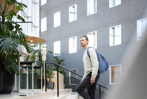 Ilari Vuores kävelee sisätilassa portaita ylös, kuvan etualalla kannettava tietokone.