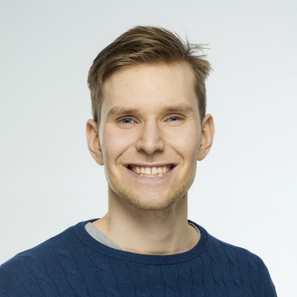 Kuva ehdokkaasta. Ruskeat hiukset, siniset silmät. Hymy, tummansininen neule.